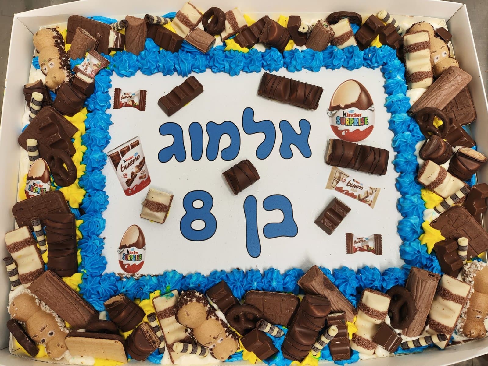 דף סוכר עם ממתקי קינדר, מסגרת קצפת כחולה וצהובה עמוסה בחטיפי שוקולד ופרלינים