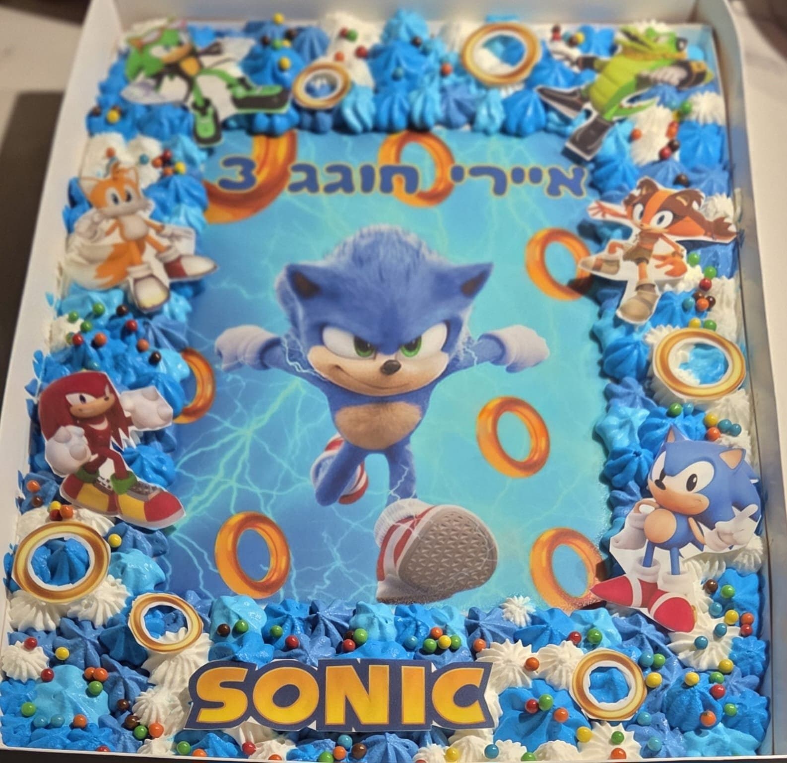 דף סוכר של סוניק על רקע תכלת עם טבעות, מסגרת קצפת כחולה וסוכריות צבעוניות