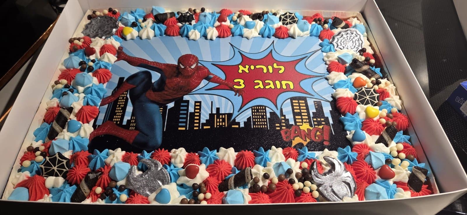 דף סוכר של ספיידרמן מעל קו הרקיע, מסגרת קצפת באדום, כחול ולבן וקורי עכביש